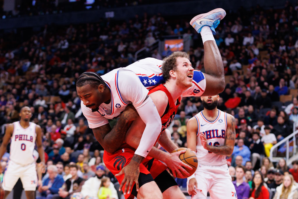 TORONTO, CANADA - OCTOBER 25: Andre Drummond #5 of the Philadelphia 76ers tumbles over the back of Jakob Poeltl #19 of the Toronto Raptors as he looks to take a shot during the second half of their NBA game at Scotiabank Arena on October 25, 2024 in Toronto, Ontario, Canada.