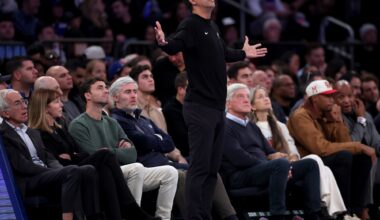 An NBA basketball coach dressed all in black stands on the sideline with his arms outstreched as if in supplication