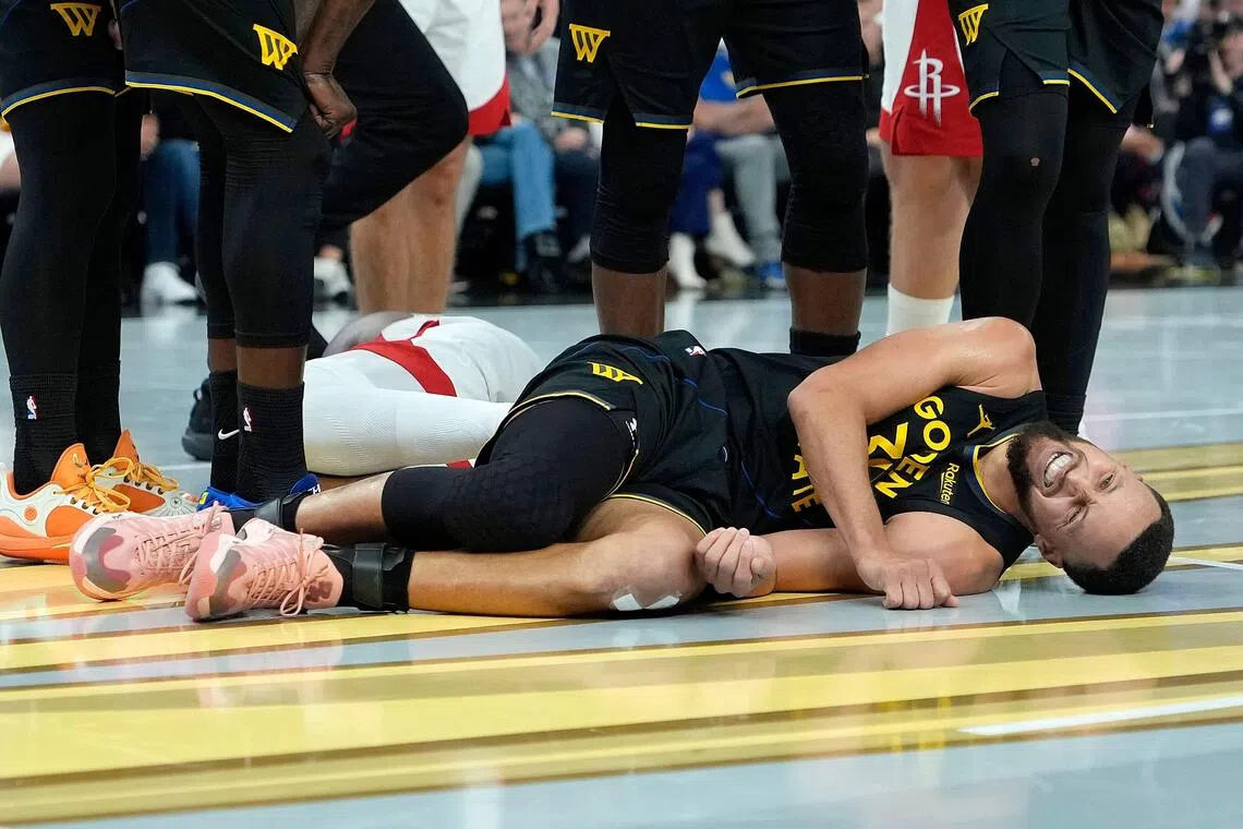 Stephen Curry of the Golden State Warriors lays on the floor in pain after colliding with Amen Thompson of the Houston Rockets.