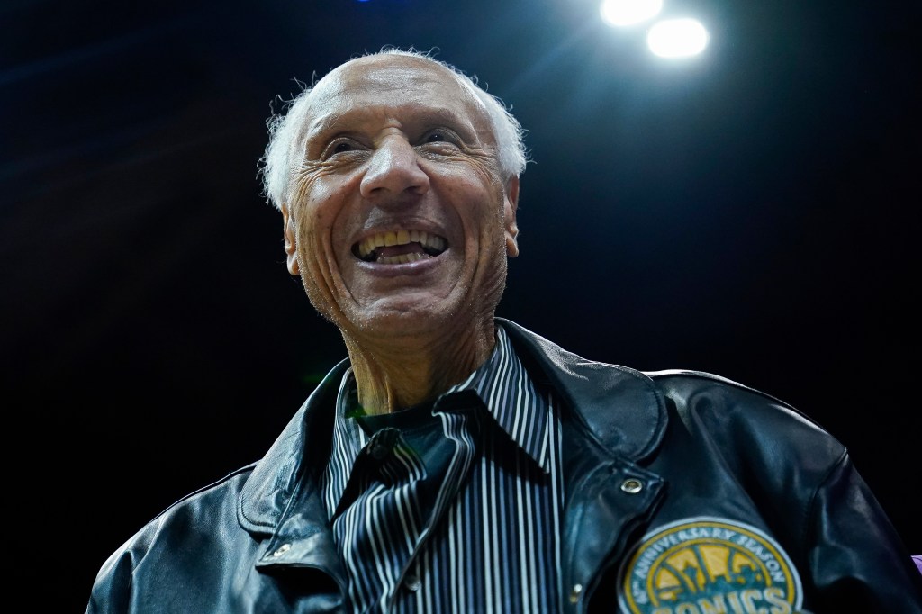 Lenny Wilkens smiling while wearing a black leather jacket over a striped shirt.
