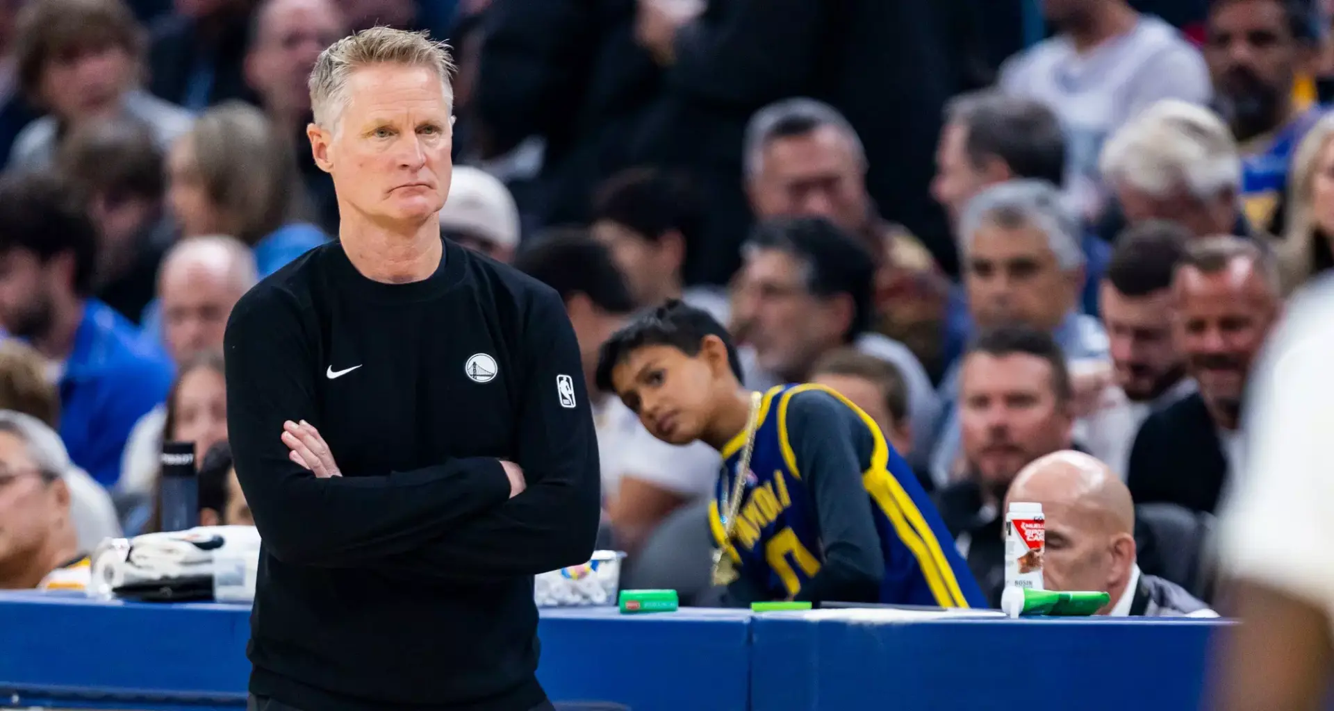 A person in scrubs, gloves, and a red cap crouches, lifting a large white face mask above their head while another mask lies on the ground.