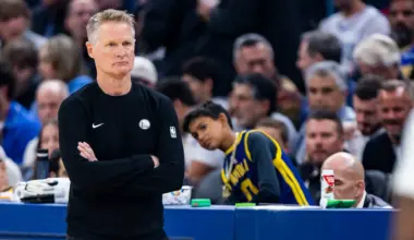 A person in scrubs, gloves, and a red cap crouches, lifting a large white face mask above their head while another mask lies on the ground.