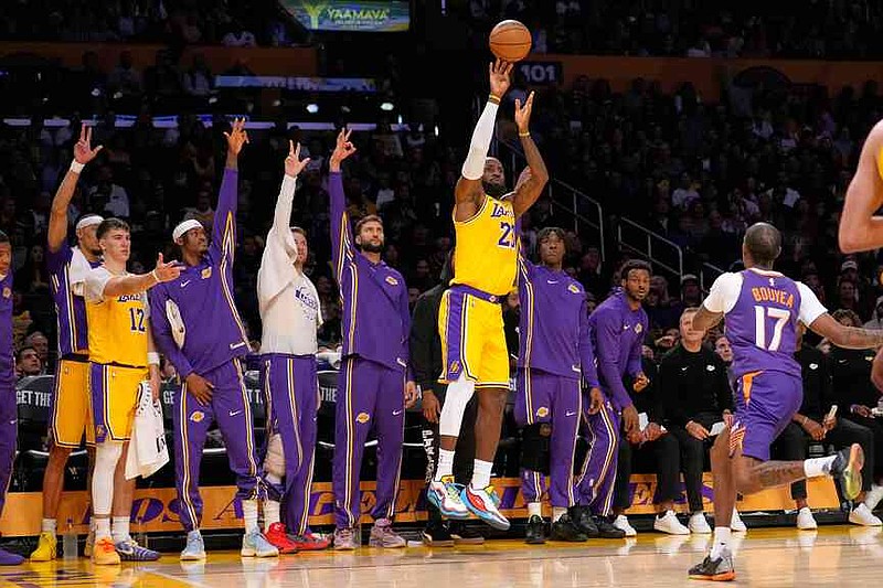 Los Angeles Lakers forward LeBron James, center, shoots as his teammates gesture from the bench while Phoenix Suns guard Jamaree Bouyea, right, defends during the first half of an NBA basketball game Monday, Dec. 1, 2025, in Los Angeles. (AP Photo/Mark J. Terrill)