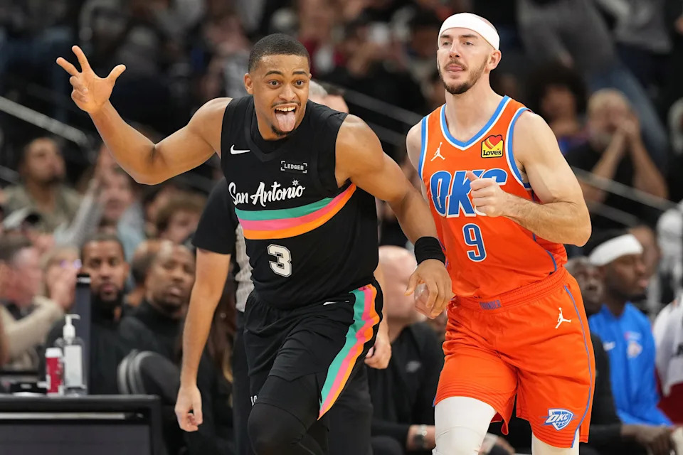 Dec 23, 2025; San Antonio, Texas, USA; San Antonio Spurs forward Keldon Johnson (3) reacts after scoring a three point basket ahead of Oklahoma City Thunder guard Alex Caruso (9) during the second half at Frost Bank Center. Mandatory Credit: Scott Wachter-Imagn Images