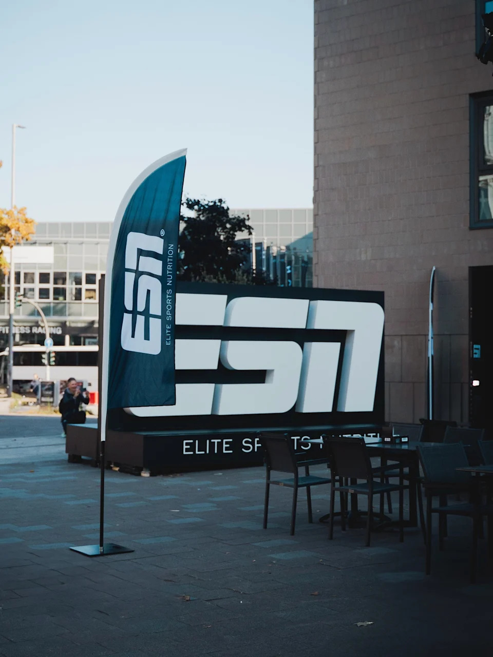 A large ESN sports nutrition display and flag set up outdoors near a modern building.
