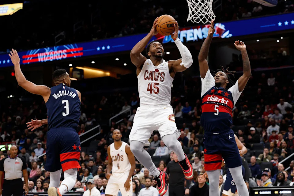Dec 12, 2025; Washington, District of Columbia, USA; Cleveland Cavaliers guard Donovan Mitchell (45) shoots the ball as Washington Wizards guard Jamir Watkins (5) and Wizards guard CJ McCollum (3) defend in the fourth quarter at Capital One Arena. Mandatory Credit: Geoff Burke-Imagn Images