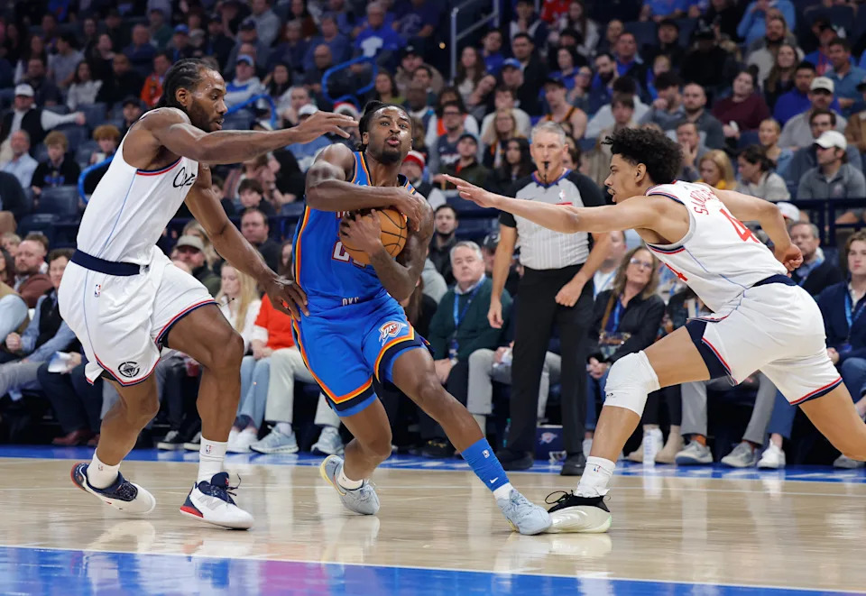 Dec 18, 2025; Oklahoma City, Oklahoma, USA; Oklahoma City Thunder guard Cason Wallace (22) drives between Los Angeles Clippers forward Kawhi Leonard (2) and guard Kobe Sanders (4) during the first quarter at Paycom Center. Mandatory Credit: Alonzo Adams-Imagn Images