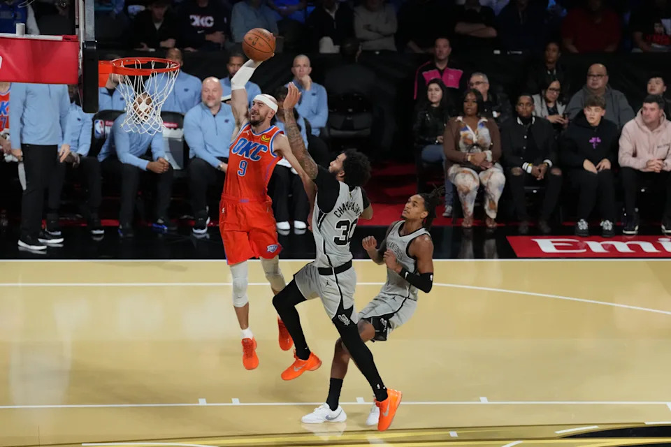 Dec 13, 2025; Las Vegas, Nevada, USA; Oklahoma City Thunder guard Alex Caruso (9) goes up for the dunk as San Antonio Spurs forward Julian Champagnie (30) defends during the second half at T-Mobile Arena. Mandatory Credit: Kirby Lee-Imagn Images