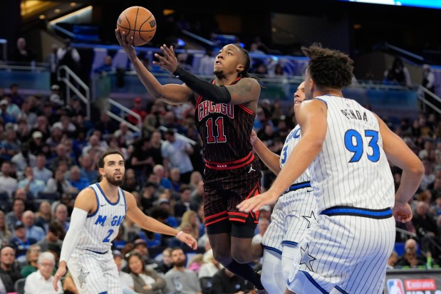 Chicago Bulls guard Ayo Dosunmu (11) makes a shot as he gets between Orlando Magic guard Tyus Jones (2), guard Desmond Bane (3) and forward Noah Penda (93) during the second half of an NBA basketball game, Monday, Dec. 1, 2025, in Orlando, Fla. (AP Photo/John Raoux)