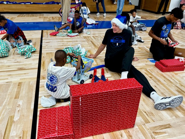 Magic center Moe Wagner helps a young kid from the New Image Youth Center in Parramore open presents during a special holiday event Wednesday night at the AdventHealth Training Center. (Jason Beede/Orlando Sentinel)