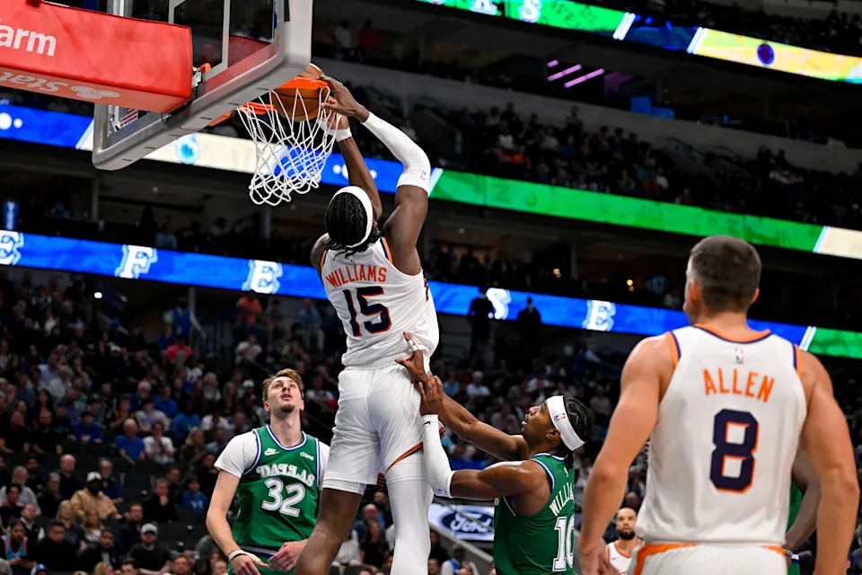 Phoenix Suns center Mark Williams (15) makes a reverse dunk as Dallas Mavericks forward Cooper Flagg (32) and guard Brandon Williams (10) looks on during the second half at the American Airlines Center in Dallas, on Nov. 12, 2025.