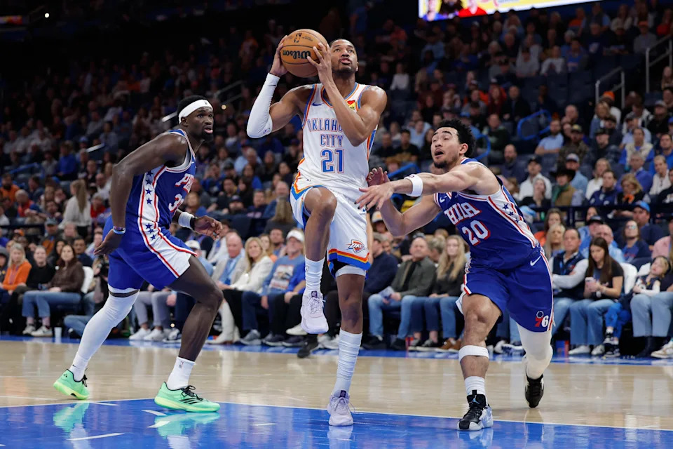 Dec 28, 2025; Oklahoma City, Oklahoma, USA; Oklahoma City Thunder guard Aaron Wiggins (21) drives between Philadelphia 76ers center Adem Bona (30) and guard Jared McCain (20) during the second half at Paycom Center. Mandatory Credit: Alonzo Adams-Imagn Images