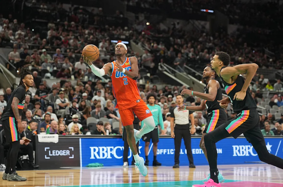 Dec 23, 2025; San Antonio, Texas, USA; Oklahoma City Thunder guard Shai Gilgeous-Alexander (2) drives to the basket between San Antonio Spurs forward Victor Wembanyama (1) and guard Stephon Castle (5) during the second half at Frost Bank Center. Mandatory Credit: Scott Wachter-Imagn Images