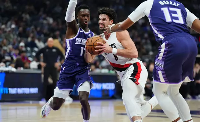 Portland Trail Blazers forward Deni Avdija (8) drives between Sacramento Kings guard Dennis Schroder, left, and forward Keegan Murray (13) during the first half of an NBA basketball game Saturday, Dec. 20, 2025, in Sacramento, Calif. (AP Photo/Alan Greth)