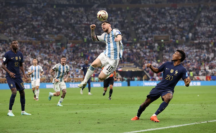 A soccer player directs the ball with his head while leaping high into the air. The stands behind him are packed.