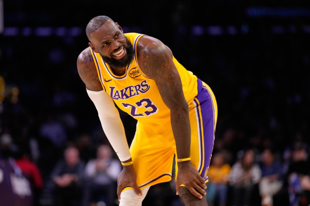 LeBron James, wearing a yellow Lakers jersey, bends over with his hands on his knees and a pained expression.