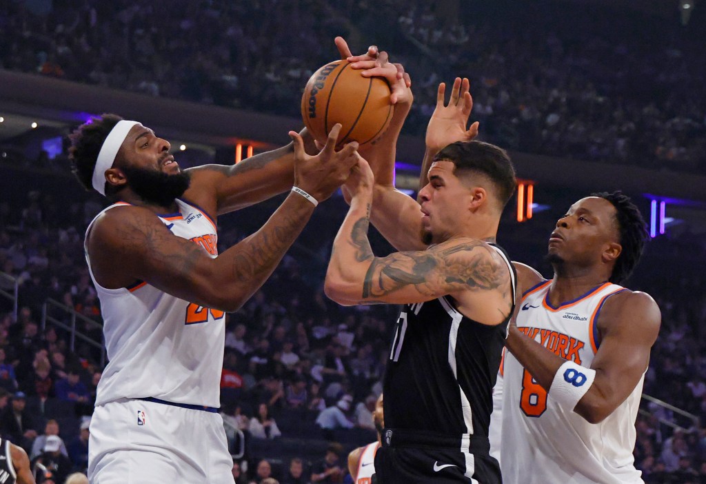 Three basketball players, two in white "New York" jerseys and one in a black "Brooklyn" jersey, are fighting for control of a basketball.