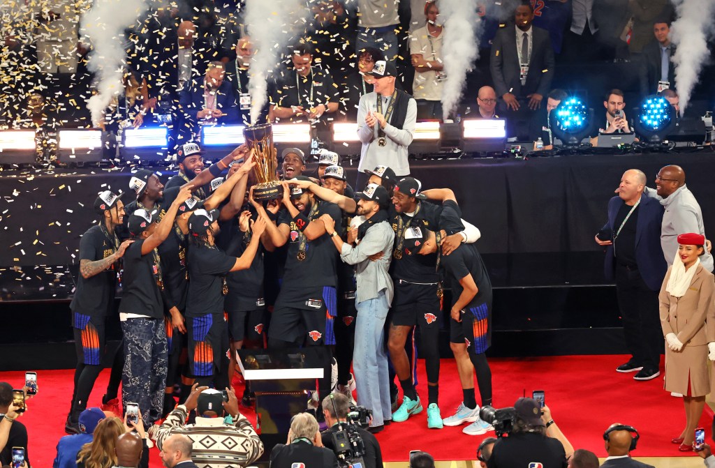 The New York Knicks basketball team celebrating with the NBA Cup championship trophy, surrounded by confetti and smoke.