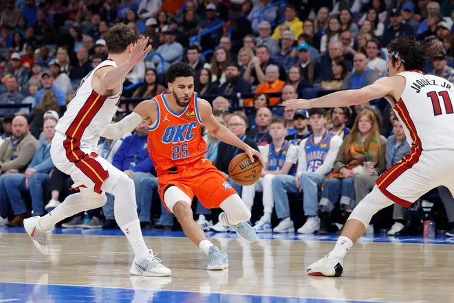Jan 11, 2026; Oklahoma City, Oklahoma, USA; Oklahoma City Thunder guard Ajay Mitchell (25) drives between Miami Heat guard Pelle Larsson (9) and guard Jaime Jaquez Jr. (11) during the second half at Paycom Center. Mandatory Credit: Alonzo Adams-Imagn Images