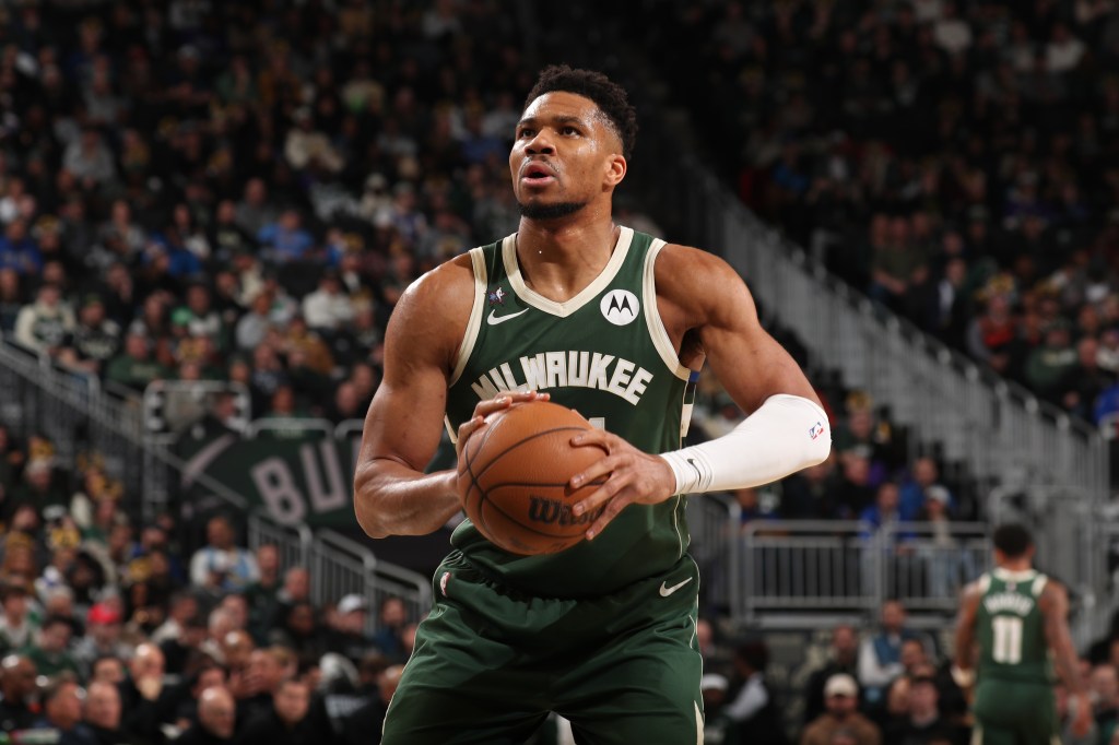 Giannis Antetokounmpo holding a basketball, wearing a green Milwaukee Bucks jersey.