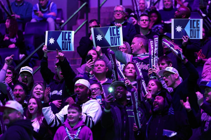 Fans at the game hold signs to protest the presence of federal agents in Minneapolis. 
