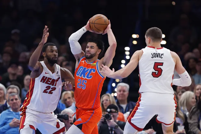 Jan 11, 2026; Oklahoma City, Oklahoma, USA; Oklahoma City Thunder guard Ajay Mitchell (25) passes in between Miami Heat forward Andrew Wiggins (22) and forward Nikola Jović (5) during the second quarter at Paycom Center. Mandatory Credit: Alonzo Adams-Imagn Images