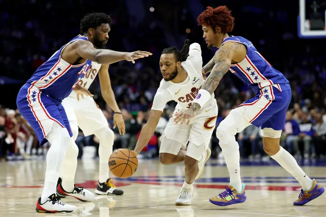 PHILADELPHIA, PENNSYLVANIA - JANUARY 14: Darius Garland #10 of the Cleveland Cavaliers drives against Joel Embiid #21 and Kelly Oubre Jr. #9 of the Philadelphia 76ers during the first half at Xfinity Mobile Arena on January 14, 2026 in Philadelphia, Pennsylvania. NOTE TO USER: User expressly acknowledges and agrees that, by downloading and or using this photograph, User is consenting to the terms and conditions of the Getty Images License Agreement. (Photo by Emilee Chinn/Getty Images)