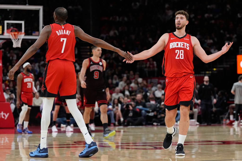 Two Houston Rockets players in red jerseys shake hands on the basketball court.