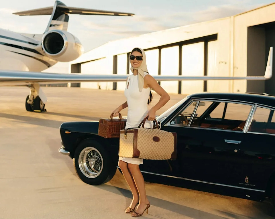 Kendall Jenner appears in a travel-themed moment from her Super Bowl commercial, styled in a minimalist look while stepping away from a vintage car.
