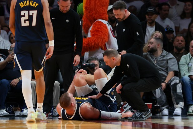 Nuggets center Nikola Jokic (15) grabs his left knee as head coach David Adelman approaches him after an injury against the Miami Heat during the second quarter at the Kaseya Center in Miami, Fla. on Dec. 29, 2025. (Photo by Sam Navarro via Imagn Images)