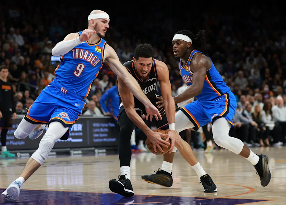 Jan 4, 2026; Phoenix, Arizona, USA; Phoenix Suns guard Devin Booker (center) drives to the basket against Oklahoma City Thunder guard Alex Caruso (9) and Luguentz Dort (5) in the second half at Mortgage Matchup Center. Mandatory Credit: Mark J. Rebilas-Imagn Images