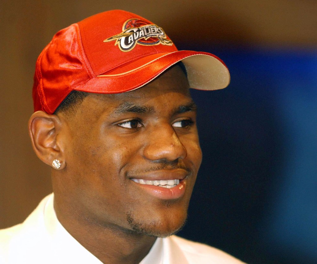 LeBron James wearing a red Cleveland Cavaliers baseball cap and smiling during the NBA Draft.
