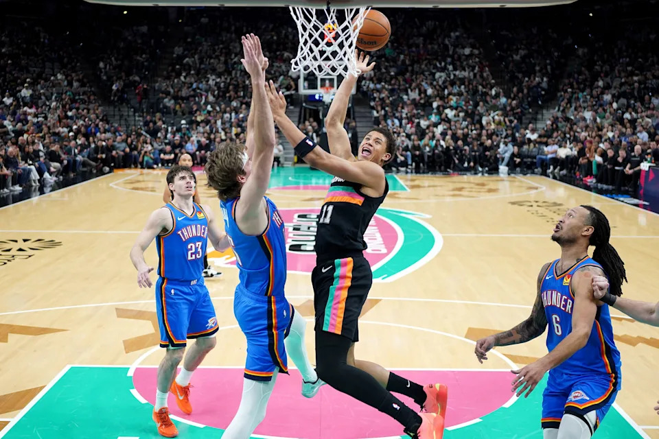 Feb 4, 2026; San Antonio, Texas, USA; San Antonio Spurs forward Carter Bryant (11) shoots over Oklahoma City Thunder center Branden Carlson (15) and forward Jaylin Williams (6) during the second half at Frost Bank Center. Mandatory Credit: Scott Wachter-Imagn Images