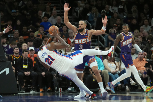 Philadelphia 76ers center Joel Embiid (21) is fouled by Phoenix Suns forward Dillon Brooks (3) as Suns guard Jalen Green (4) looks on during the second half of an NBA basketball game Saturday, Feb. 7, 2026, in Phoenix. (AP Photo/Ross D. Franklin)