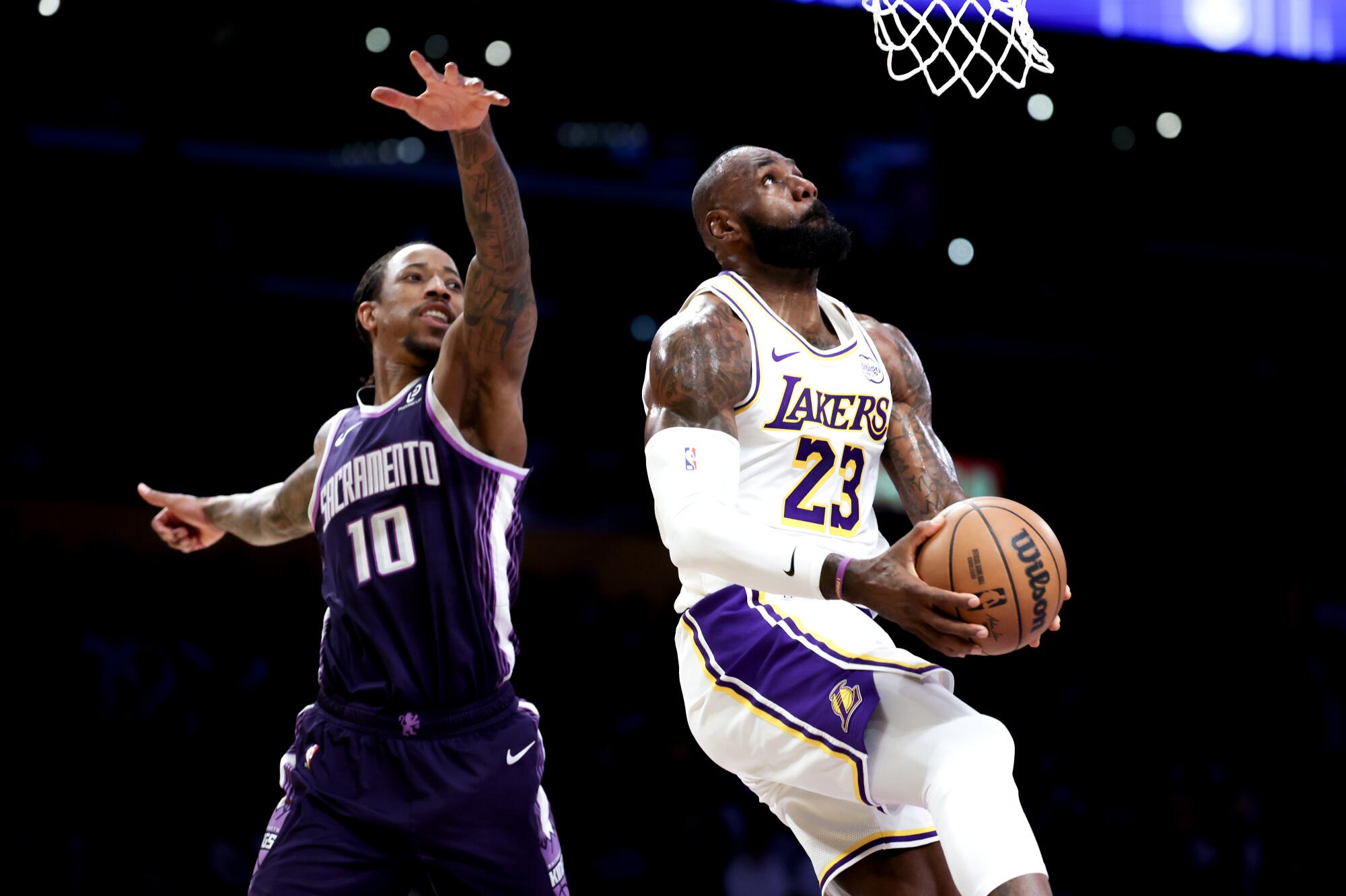 Lakers forward LeBron James, right, glides past Kings forward DeMar DeRozan for a reverse dunk during a game in December.