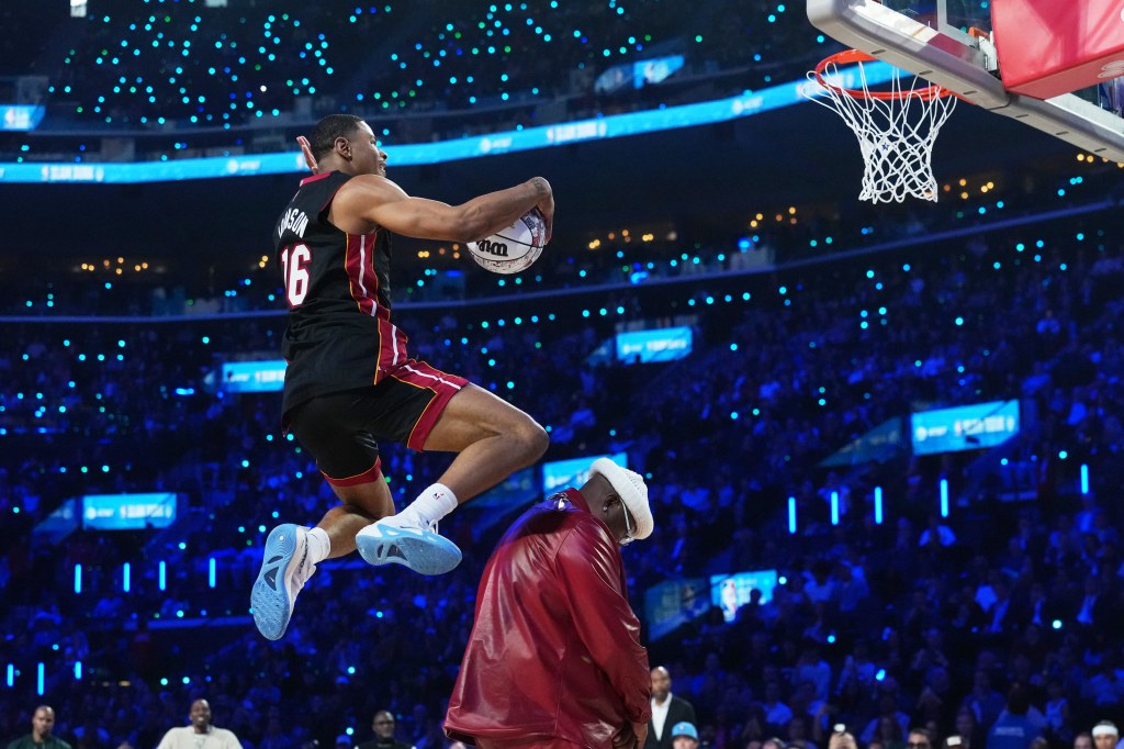 NBA player Mac McClung jumps over a man to dunk the basketball.