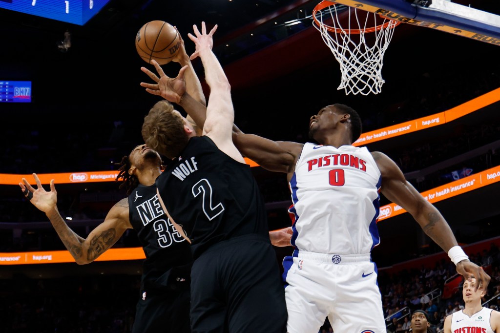 Three basketball players jump for a rebound near the basket.