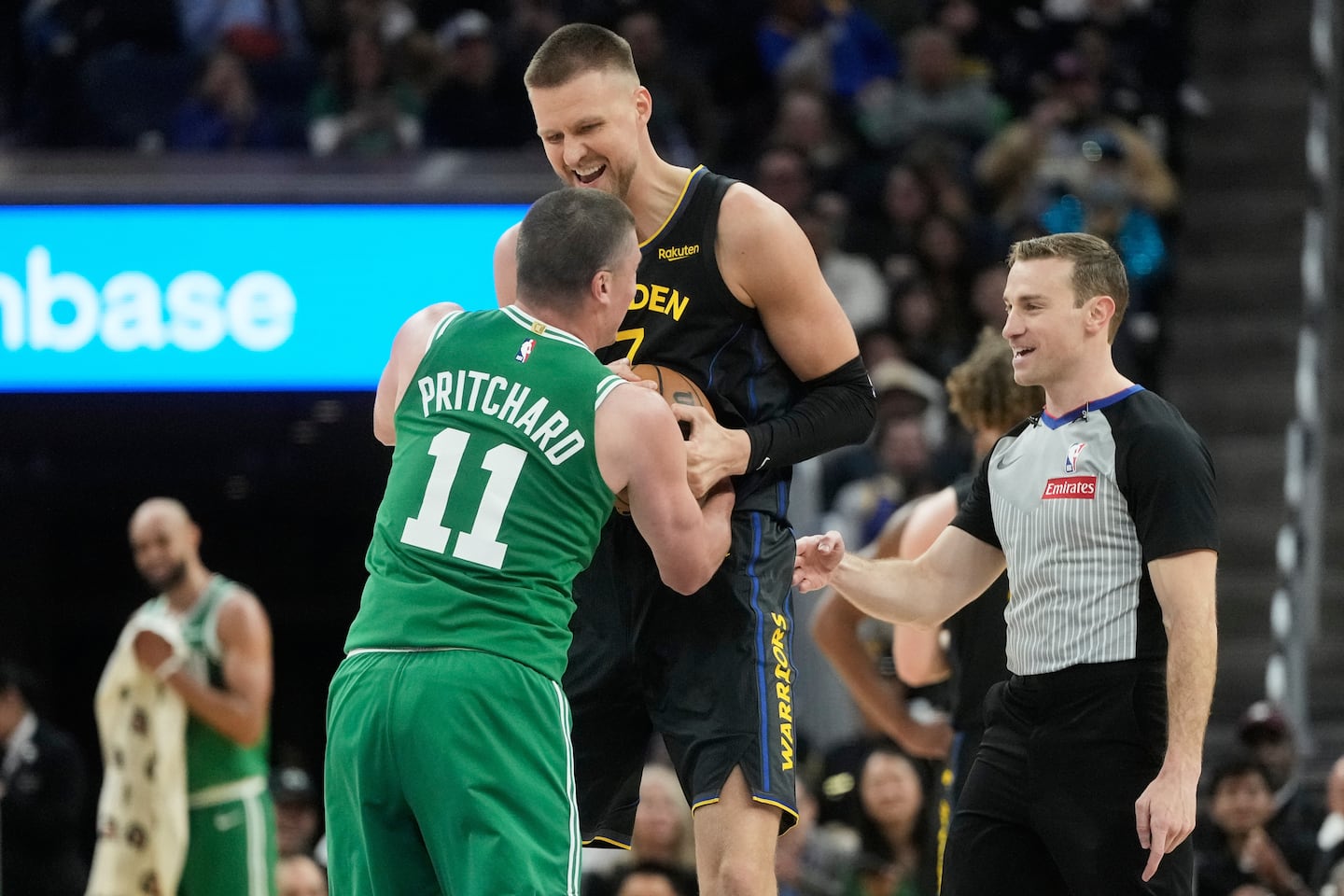 Golden State Warriors center Kristaps Porziņģis smiles while wrestling for the ball with Boston Celtics guard Payton Pritchard.