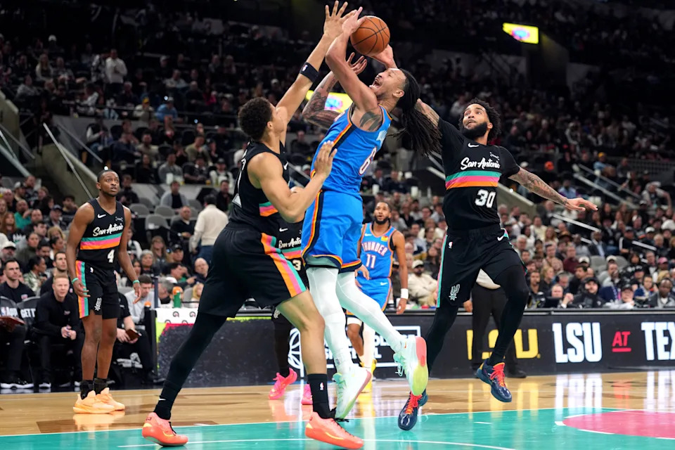Feb 4, 2026; San Antonio, Texas, USA; Oklahoma City Thunder forward Jaylin Williams (6) drives to the basket against San Antonio Spurs forwards Carter Bryant (11) and Julian Champagnie (30) during the second half at Frost Bank Center. Mandatory Credit: Scott Wachter-Imagn Images