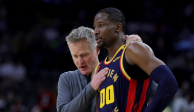 A coach speaks closely to a Golden State Warriors player wearing jersey number 00 during a game, with the player listening intently.