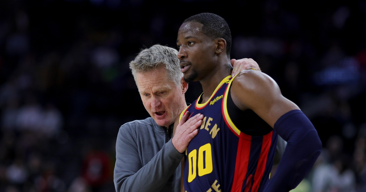 A coach speaks closely to a Golden State Warriors player wearing jersey number 00 during a game, with the player listening intently.