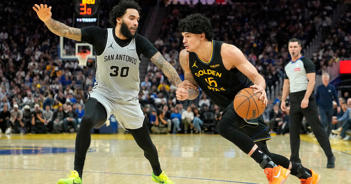 A Golden State player dribbles past a San Antonio defender in a closely contested basketball game with a referee in the background.