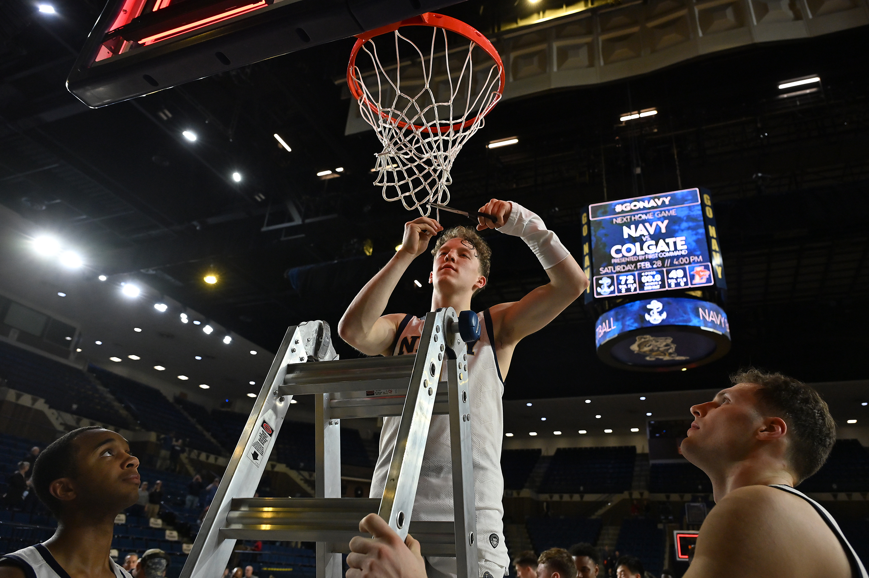 Navy Midshipmen guard Austin Benigni #1 cuts a piece of the net down after the win. The Navy Midshipmen defeated the Lehigh Mountain Hawks, 72-49, to become the Patriot League Regular Season Champions in men's NCAA basketball. (Paul W. Gillespie/Staff)
