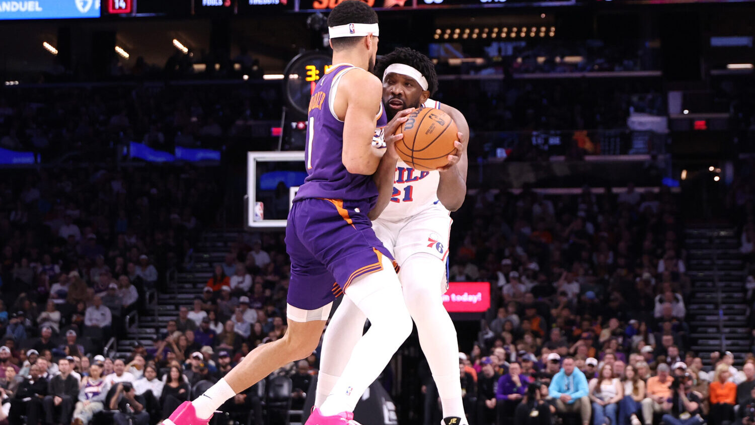 Devin Booker #1 of the Phoenix Suns fouls Joel Embiid #21 of the Philadelphia 76ers during the firs...