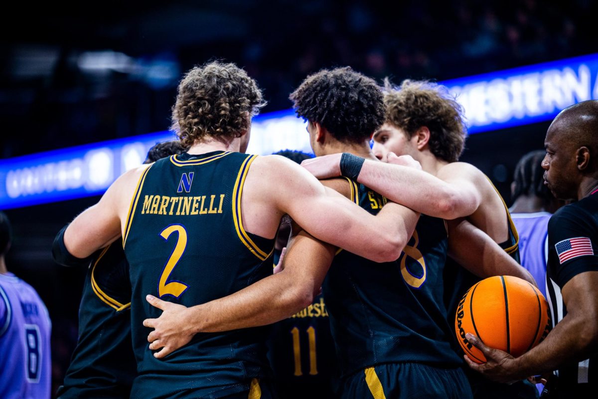 A group of Northwestern players huddle together with their backs turned to the camera.