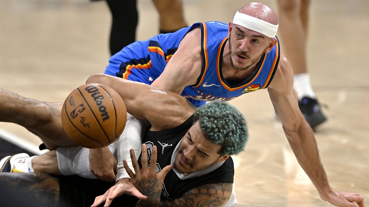 San Antonio Spurs forward Jeremy Sochan, bottom, and Oklahoma City Thunder guard Alex Caruso fight for possession during the first half of an NBA basketball game, Sunday, March 2, 2025, in San Antonio. (AP Photo/Darren Abate)