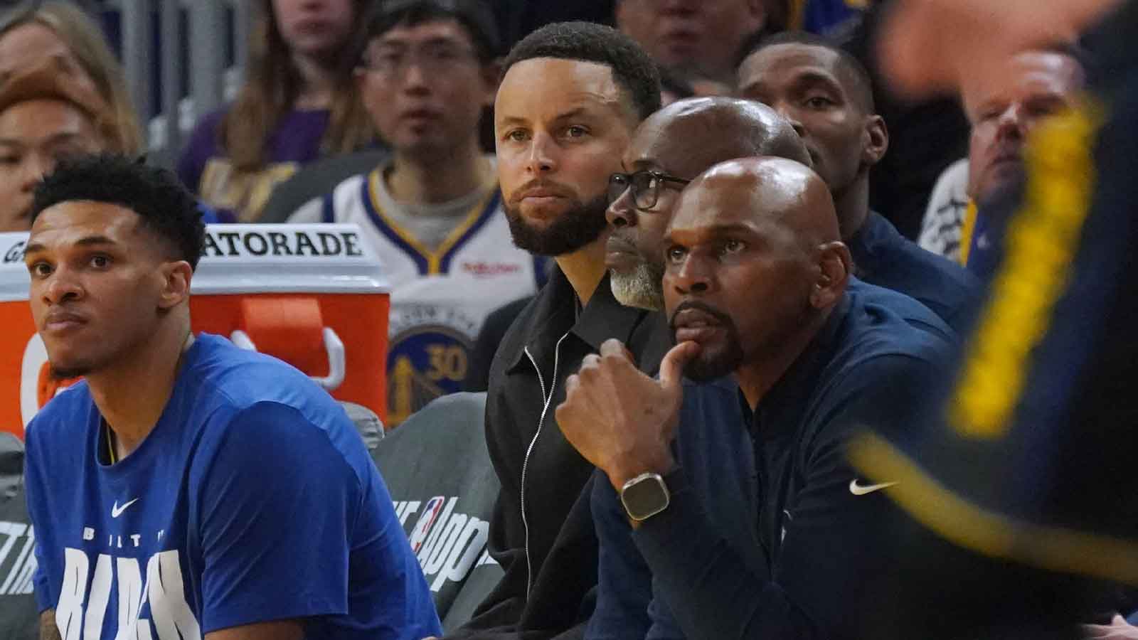 Golden State Warriors guard Will Richard (3) and guard Stephen Curry (30) watch from the bench, sitting next to assistant coaches Kris Weems and Jerry Stackhouse in the first quarter during a game against the Denver Nuggets at Chase Center.