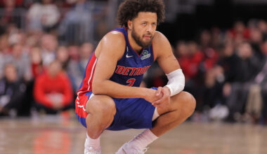 Cade Cunningham, wearing a blue Detroit Pistons jersey, an afro, and a beard, crouches on a basketball court as if in a baseball catcher's stance.