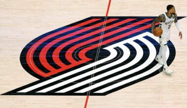 A basketball player from the Milwaukee Bucks dribbling on a court with the Portland Trail Blazers logo at center court.
