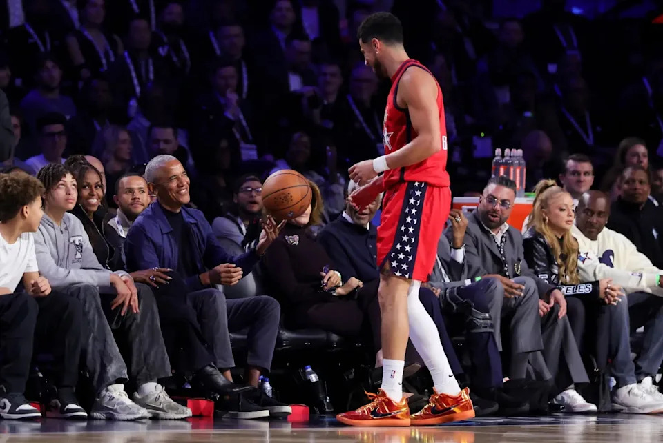 Barack Obama shares a lighthearted moment courtside after catching a loose ball during the NBA All-Star Game as Michelle and Sasha look on.